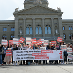 Un groupe d’environ 50 personnes portant des panneaux et une banderole devant le Palais fédéral à Berne. Sur la banderole, on peut y lire en trois langues «Pas touche au congé du dimanche!».