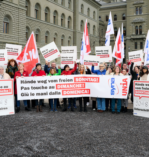 Menschen halten ein Transparent und Plakate in die Luft, auf denen «Hände weg vom freien Sonntag» in Deutsch, Französisch und Italienisch steht.