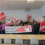 Un gruppo di persone si riunisce dietro uno striscione con la scritta «Giù le mani dalla domenica libera». Tengono in mano cartelli e sventolano bandiere Unia.