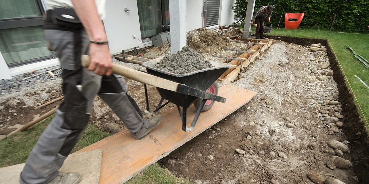 Ein Gärtner schiebt eine Karrette über eine Holzrampe auf eine neu entstehende Terrasse.