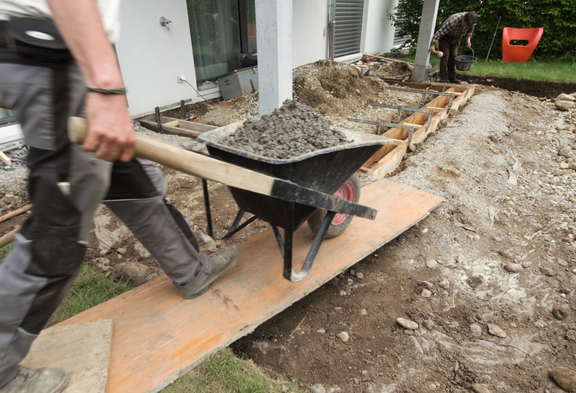 Un paysagiste pousse une brouette sur une rampe en bois sur une terrasse en construction.