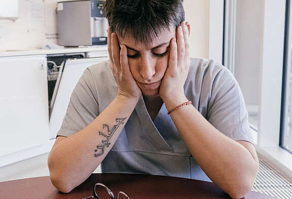 Une travailleuse du care se tient la tête dans les mains lors d’une pause sur son lieu de travail. Les conditions de travail dans les soins de longue durée et l’accompagnement sont difficiles.