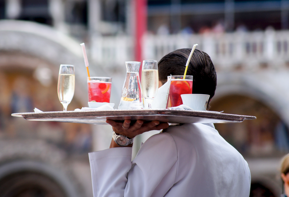 Ein Kellner von hinten mit einem Tablett voller Getränke.