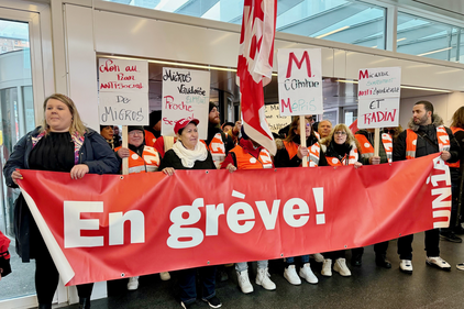 Une vingtaine d'employés de Micarna avec une banderole sur laquelle est inscrite «En grève» et des pancartes qu'ils tiennent en l'air.