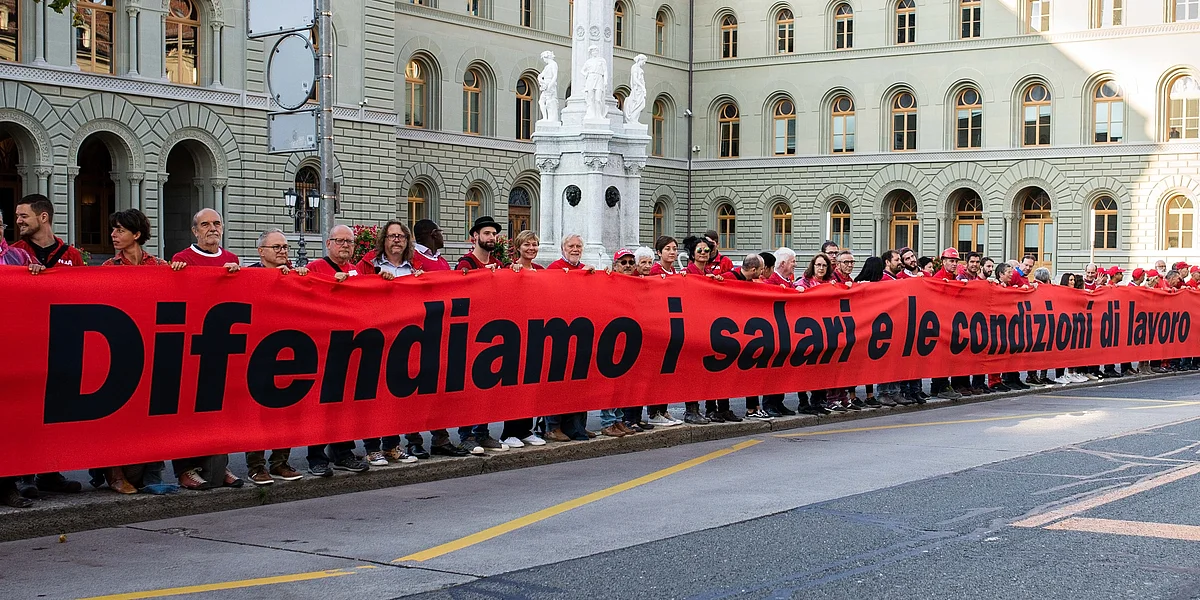 Una lunga catena umana manifesta con un grande striscione rosso con la scritta «Difendiamo i salari e le condizioni di lavoro» per diritti del lavoro forti nel quadro delle relazioni tra Svizzera e UE.