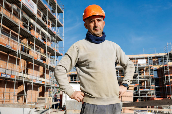 Daniel, travailleur de la construction d'Argovie, se tient sur un chantier avec son casque orange sur la tête.