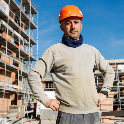 Daniel, travailleur de la construction d'Argovie, se tient sur un chantier avec son casque orange sur la tête.