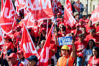 Demo-Teilnehmende mit roten Demo-T-Shirts und Mann mit Helm und Schild: "Faire Löhne"