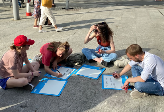 Addette e addetti alle cure seduti per terra scrivono dei cartelli in occasione di un’azione di Unia.