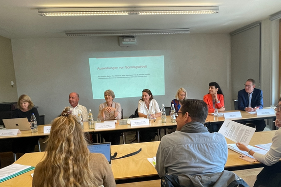 Photo de la conférence de presse de l’Alliance pour le dimanche. Les intervenant-e-s sont assis à une table de conférence. On peut voir devant eux des plaquettes avec leurs noms et, derrière eux, un écran où sont projetés les contenus de l’étude.