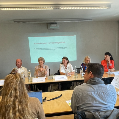 Foto der Medienkonferenz der Sonntagsallianz. Die Referent:innen sitzen gemeinsam an einem Vorstandstisch. Vor ihnen stehen Namenstafeln, hinter ihnen ist die Projektion eines Beamers mit Studieninhalten zu sehen.