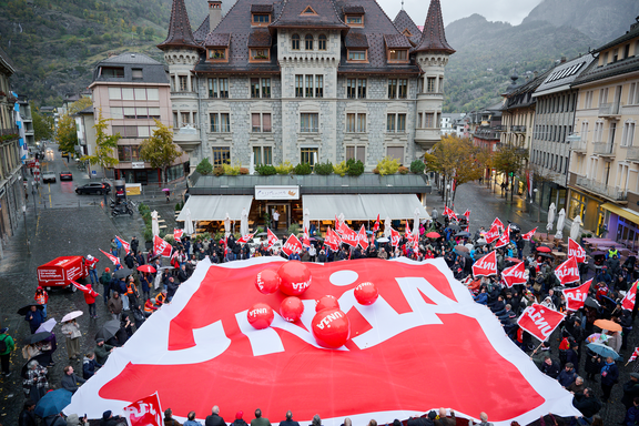 Action sur la Stadtplatz de Brigue: les délégué-e-s au congrès d'Unia tendent un énorme drapeau d'Unia sur lequel rebondissent des balles aux couleurs du syndicat.