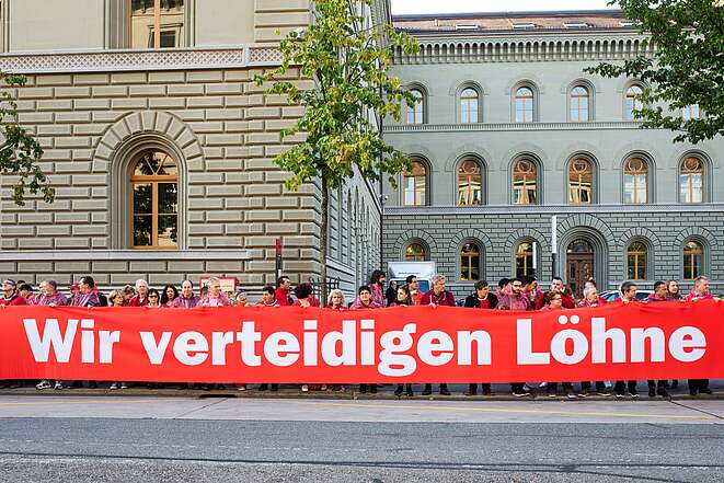 Unia-Aktivist:innen tragen ein Transparent in der Form einer roten Linie für den Lohnschutz.