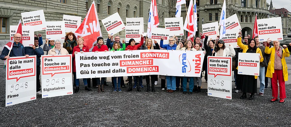 Vor dem Bundeshaus protestieren Menschen mit mehrsprachigen Plakaten, Transparenten und Unia-Fahnen gegen Sonntagsarbeit und fordern den Schutz des freien Sonntags.