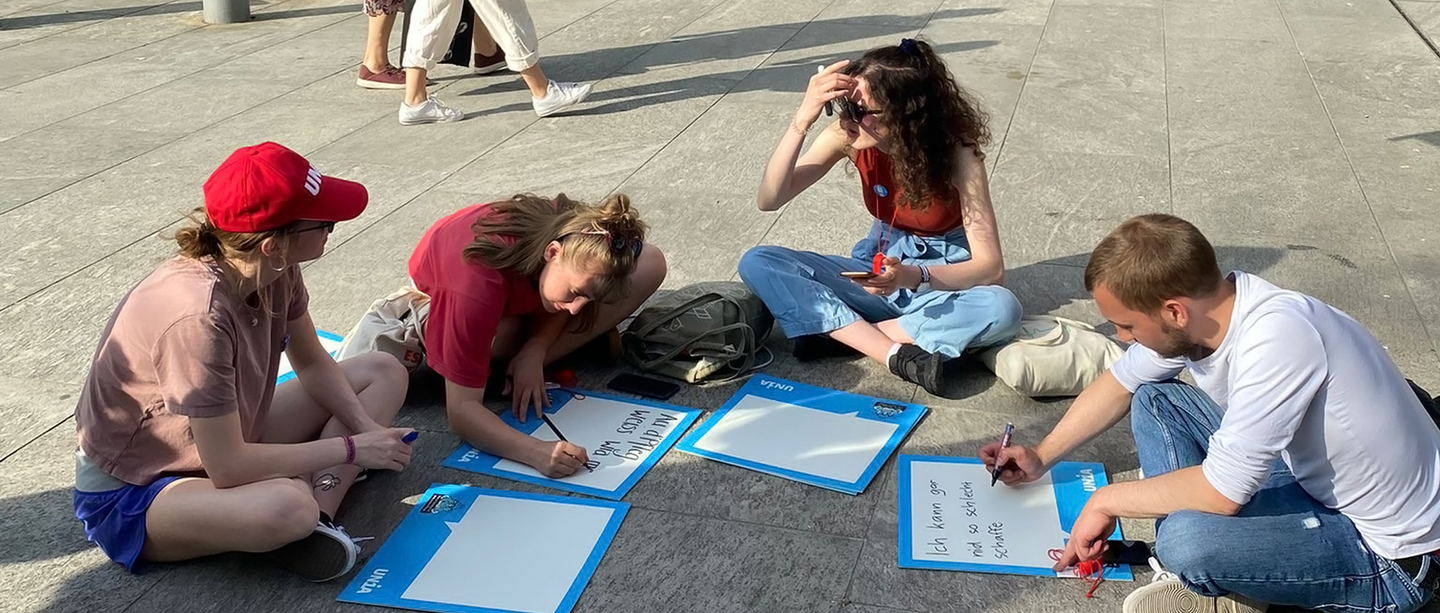 Addette e addetti alle cure seduti per terra scrivono dei cartelli in occasione di un’azione di Unia.