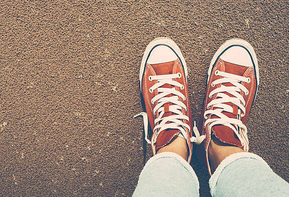 Blick von oben auf ein Paar Füsse in roten Chucks allein auf der Strasse