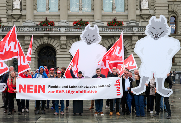 Unia-Aktivist:innen mit Wölfen aus Karton und einem Transparent vor dem Bundeshaus: 