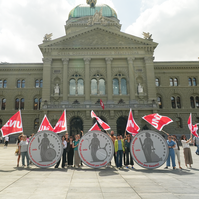 Des militant-e-s d'Unia se tiennent près de trois pièces de monnaie géantes avec l'inscription «Halte aux baisses de salaire imposées par la loi» devant le Palais fédéral à Berne. 
