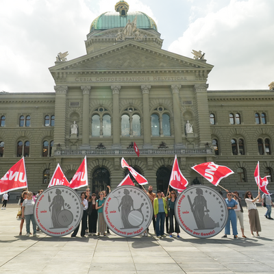 Unia-Aktivist:innen vor dem Bundeshaus in Bern halten drei übergrosse Münzen mit Helvetia und der Aufschrift «Stopp Lohnsenkungen per Gesetz» in den Landessprachen.