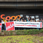 Un gruppo di 50 persone innalza uno striscione, bandiere, cartelli di cartone e grandi lettere ritagliate che riproducono il logo aziendale di Coop. Alzano il pugno al cielo e trasmettono un’immagine sindacale e combattiva. Lo slogan dello striscione è: «Più protezione grazie a un CCL forte: il nostro futuro, i nostri diritti»