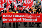 es manifestants avec des drapeaux d'Unia et une banderole disant: «Pas de licenciements chez Swiss Steel/Steeltec!». Certains portent des vêtements de travail et des casques.