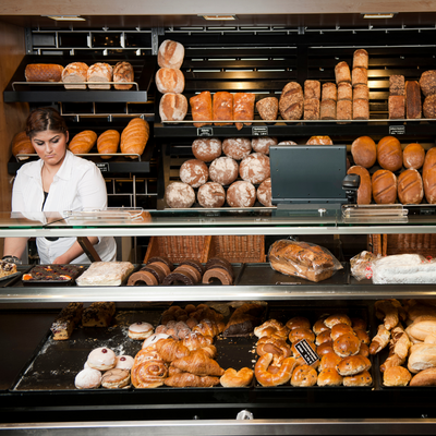 Una dipendente di una panetteria si trova dietro un espositore con panini e dolci.