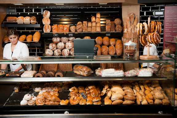 Una dipendente di una panetteria si trova dietro un espositore con panini e dolci.