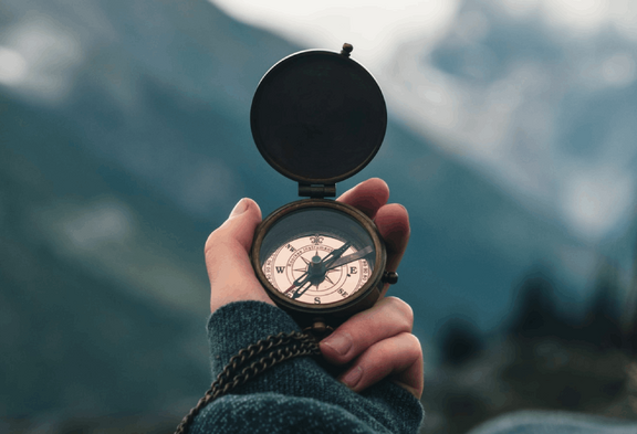 Une main tient une boussole dans un environnement de montagnes