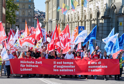 Striscione della manifestazione: "È ore di aumentare i salari" in 3 lingue