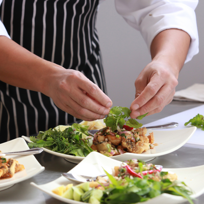 Una persona con grembiule pulito e camicia bianca prepara un piatto di insalata.