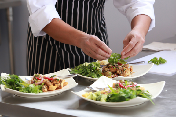 Una persona con grembiule pulito e camicia bianca prepara un piatto di insalata.