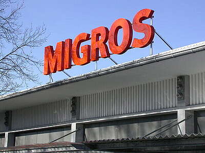 Il logo arancione di Migros sul tetto di un edificio industriale.
