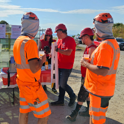 Due operai di un cantiere guardano i sindacalisti che allestiscono lo stand informativo