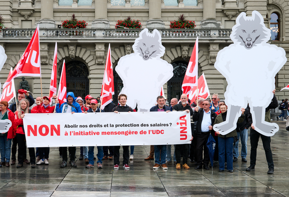 Des activistes d'Unia tiennent des pancartes en carton avec des loups déguisés en moutons et une banderole sur laquelle est écrit: 