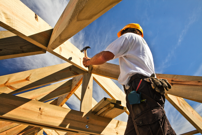 Ein Holzbau-Arbeiter steht auf einer Leiter und arbeitet an einem Haus.