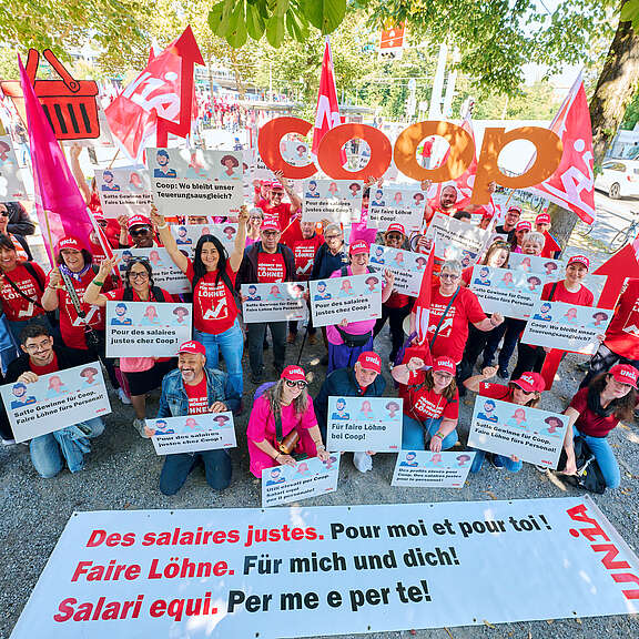 Lavoratrici e lavoratori di Coop con magliette e berretti rossi Unia tengono cartelli con rivendicazioni come 