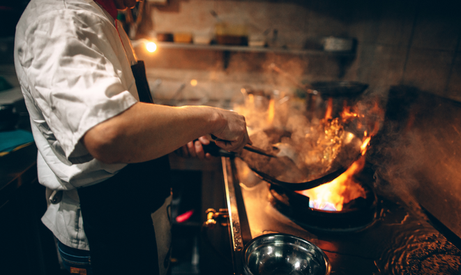 Un cuisinier en train de flamber de la nourriture dans une poêle