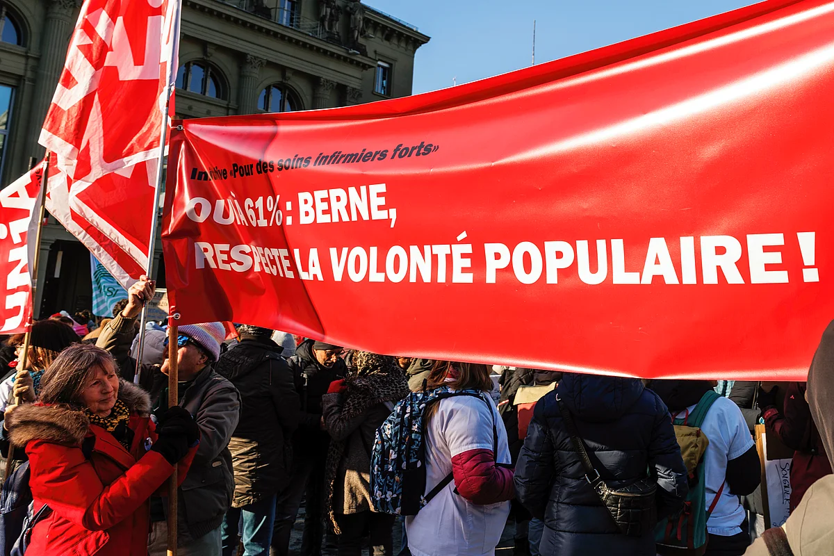 Dans la manifestation pour des soins de qualité, gros plan sur une banderole dont le texte dit "Initiative «Pour des soins infirmiers forts» OUI À 61%: BERNE, RESPECTE LA VOLONTÉ POPULAIRE!"