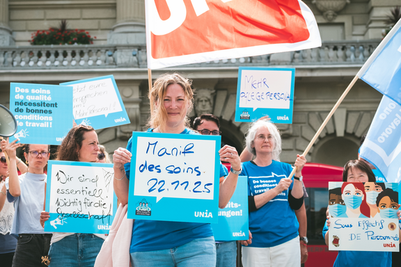 Menschen an eine Pflege-Demo mit Schildern auf denen steht: 