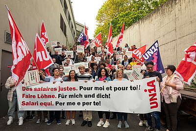 Membri del gruppo professionale Coop posano di fronte a un edificio con striscioni e bandiere Unia: 