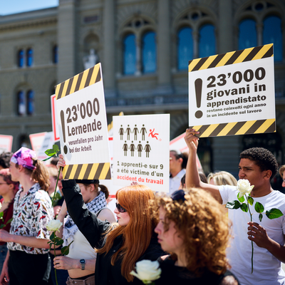 Davanti al Palazzo federale si vedono persone che tengono cartelli con le scritte «Ogni anno muoiono 3 apprendisti a seguito di un infortunio sul lavoro» e «Ogni anno 23 000 apprendisti sono vittime di un infortunio sul lavoro», in italiano, francese e in tedesco.