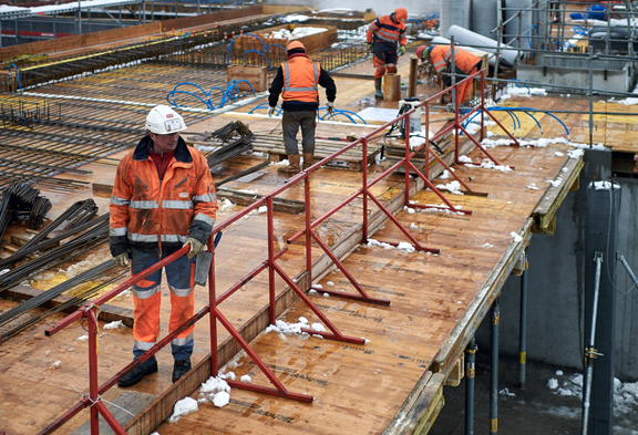 Des maçons portant des vêtements de protection orange et des casques travaillent sur un chantier.