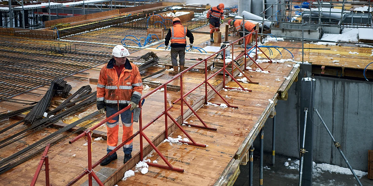 Des maçons portant des vêtements de protection orange et des casques travaillent sur un chantier.