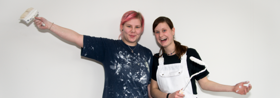 Deux jeunes femmes peintres devant un mur.