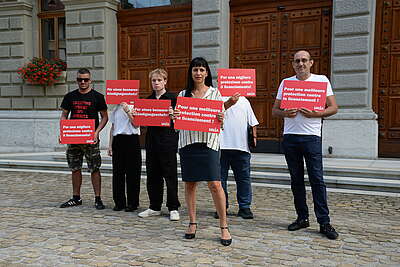 Des personnes debout sur la Place fédérale, dont Vania Alleva, tiennent des panneaux rouges avec des inscriptions blanches pour une meilleure protection contre le licenciement en Suisse.
