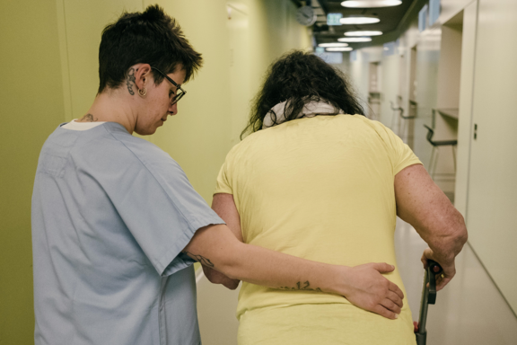 Pflegende hilft einer älteren Frau beim Gehen