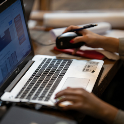 Una persona lavora al computer portatile su un tavolo pieno di oggetti.