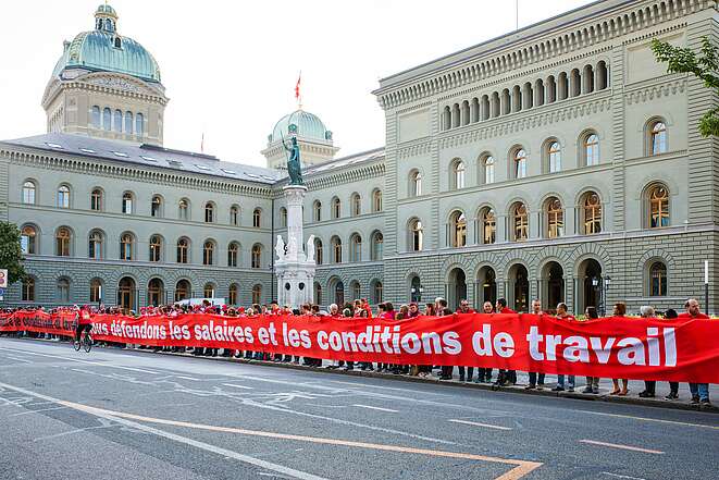 Des activistes d’Unia portent une banderole sous forme d’une ligne rouge pour la protection des salaires