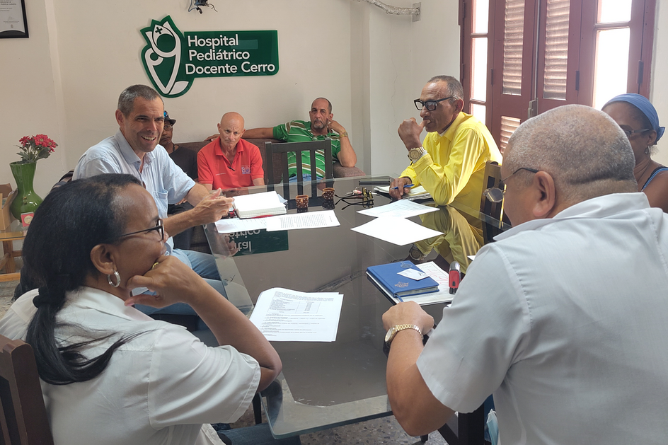 Im Krankenhaus El Cerro in Havanna sitzen Mitarbeiter:innen mit Beat Schmid, dem Co-Präsidenten des Vereins für medizinische Hilfe in Mittelamerika (AMCA) und Mitglied von mediCuba, an einem Tisch zusammen.
