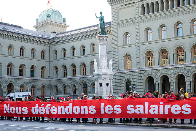 Des personnes tiennent une longue banderole près de la place fédérale à Berne avec les mots « Nous défendons les salaires ».